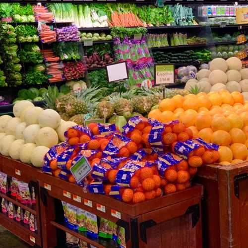 A vibrant display of fresh fruits and vegetables, including melons, oranges, and greens, in a grocery store.