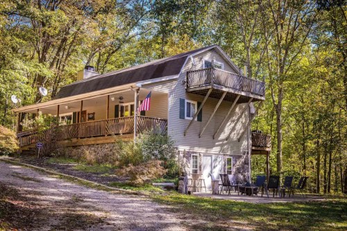 A two-story house surrounded by trees, featuring a balcony, porch, and outdoor seating area.