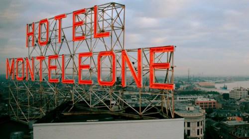 Neon sign for Hotel Monteleone atop a building, with a cloudy sky and cityscape in the background.