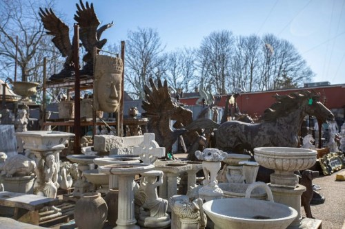A collection of various sculptures and garden ornaments displayed outdoors, including horses, a large head, and decorative pieces.