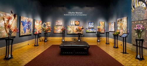 Art gallery featuring vibrant paintings and floral arrangements, showcasing the "Ubuhle Women" exhibition.