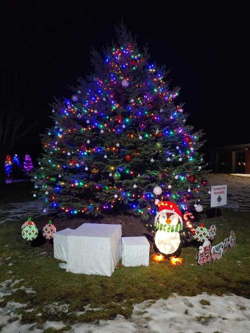 A brightly lit Christmas tree with colorful ornaments, surrounded by snow and a festive snowman decoration.