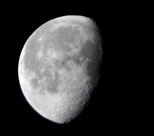 A close-up view of a half-moon against a black sky, showcasing its craters and surface details.
