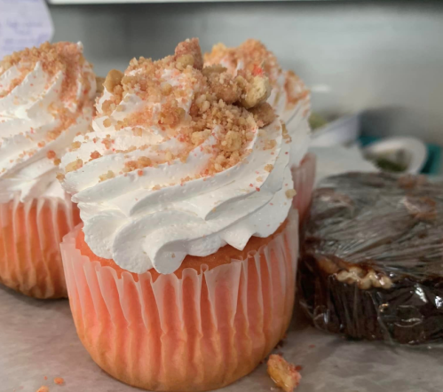 Two frosted cupcakes with crumbled topping, one orange and one chocolate, on a countertop.