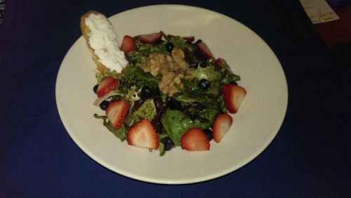 A colorful salad with mixed greens, strawberries, blueberries, and a dollop of whipped cream on the side.