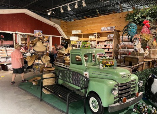 A vintage green truck filled with straw hats, set in a rustic store with wooden shelves and decor.