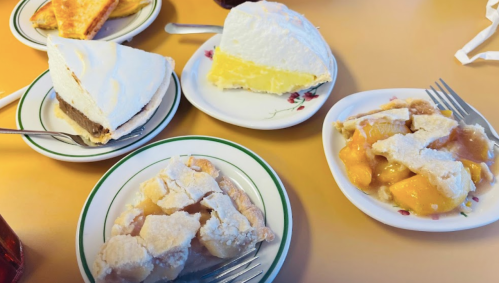 A table with four dessert plates: chocolate cream pie, lemon pie, and a fruit dessert with peaches and meringue.
