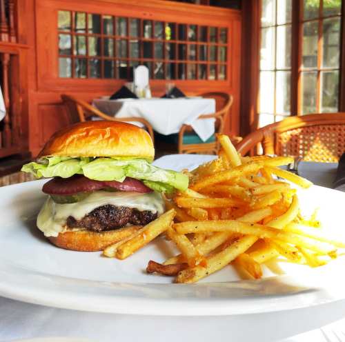 A juicy burger with lettuce, pickles, and cheese, served with a side of crispy French fries on a white plate.