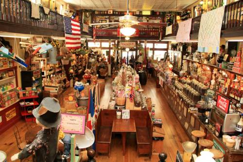 A vibrant, vintage general store filled with various goods, featuring wooden floors and an American flag hanging above.