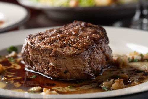 A perfectly cooked steak on a plate, glistening with sauce and garnished with herbs.