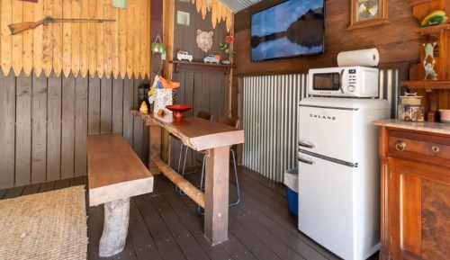 Cozy cabin interior featuring a wooden table, vintage fridge, and a TV on the wall, with rustic decor.