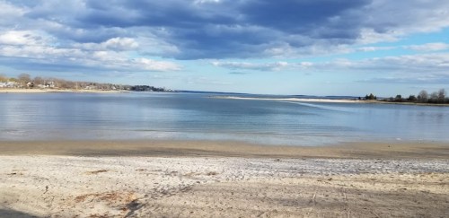 A serene beach scene with calm water, gentle waves, and a cloudy sky in the background.