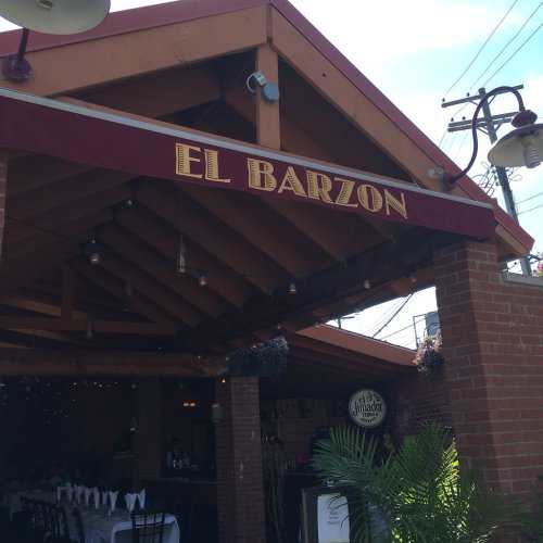 Exterior of El Barzon restaurant with a maroon awning, string lights, and a sunny sky in the background.