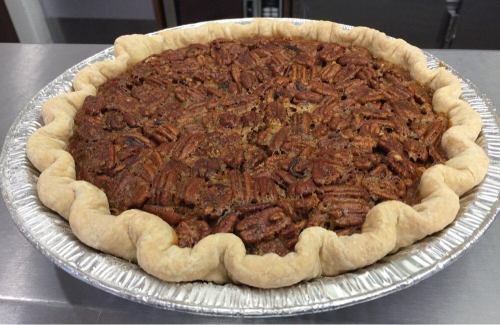 A freshly baked pecan pie in a silver pie dish with a golden, fluted crust.