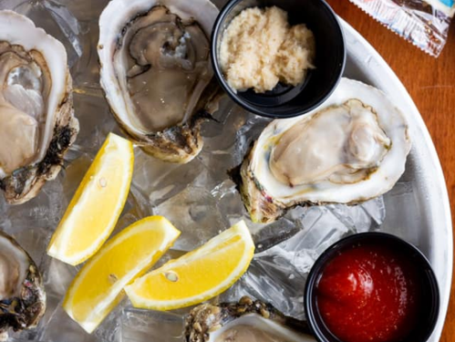 A platter of fresh oysters on ice, served with lemon wedges, horseradish, and cocktail sauce.