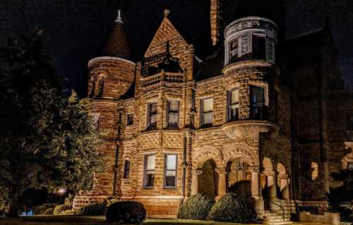 A beautifully lit historic stone mansion at night, featuring turrets and intricate architectural details.