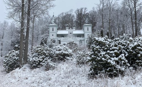 A white castle-like structure surrounded by snow-covered trees and shrubs in a winter landscape.