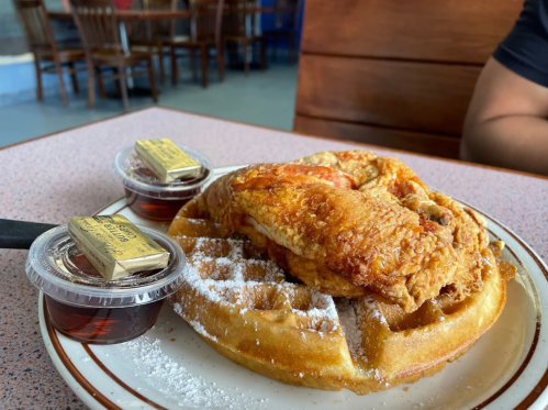 A plate with a golden waffle topped with crispy fried chicken, served with syrup and butter on the side.