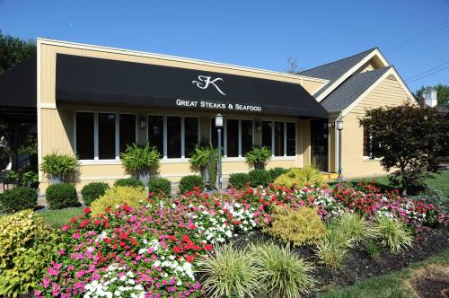 Exterior of a restaurant with a black awning, surrounded by colorful flower beds and greenery on a sunny day.