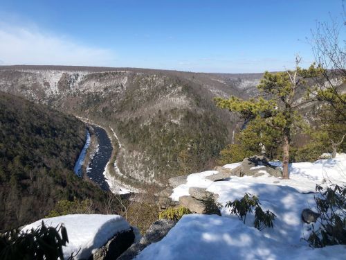 A scenic view of a snow-covered valley with a winding river, surrounded by mountains under a clear blue sky.