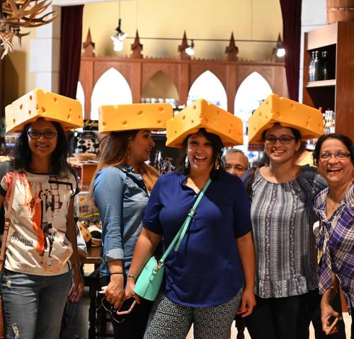 A group of five people wearing large cheese hats, smiling and posing together in a store.