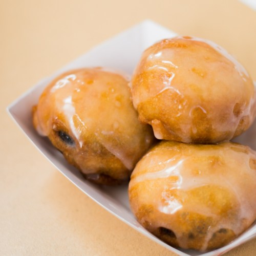 Three glazed, golden-brown doughnut holes in a white dish, with a shiny icing coating.