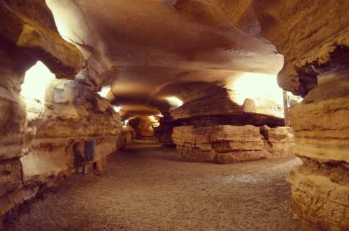 A dimly lit cave with smooth, curved rock formations and a sandy floor, creating a serene underground passage.