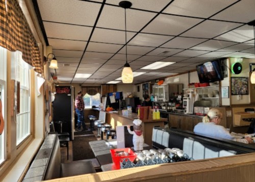 Interior of a cozy diner with booths, a counter, and patrons enjoying their meals. Bright lighting and a welcoming atmosphere.