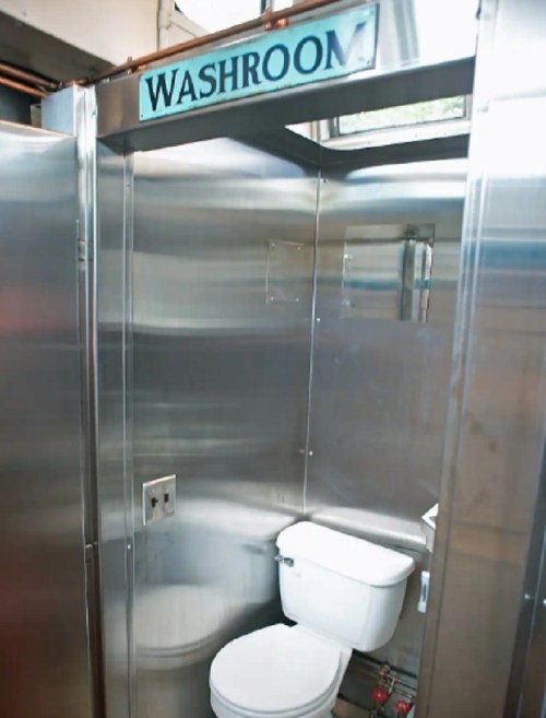 A clean, stainless steel washroom with a toilet and a sign above indicating "WASHROOM."
