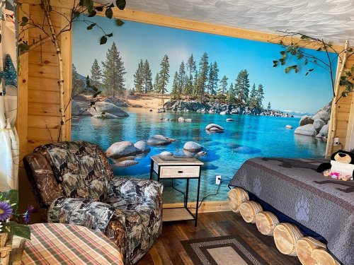 Cozy room with a nature mural of a lake, rocks, and trees, featuring a patterned chair and wooden furniture.