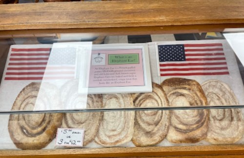 A display case with Elephant Ear pastries and two small American flags, with a sign explaining the treat.