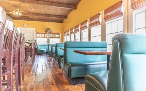Interior of a restaurant featuring green booths, wooden floors, and large windows with natural light.