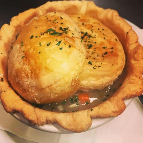 A bowl of hearty chicken pot pie with two golden, flaky pastry tops and a sprinkle of parsley.