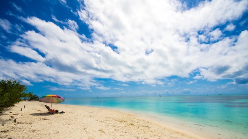 A serene beach scene with a colorful umbrella, soft sand, and calm turquoise waters under a partly cloudy sky.