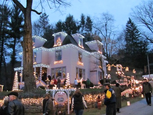 A beautifully decorated house with festive lights, surrounded by trees and people enjoying the holiday atmosphere.