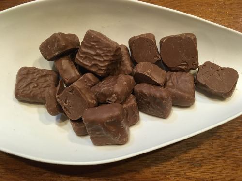 A white dish filled with assorted chocolate-covered candies, varying in shape and size, on a wooden surface.