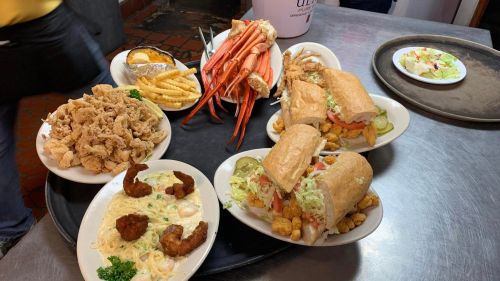 A table filled with seafood dishes, including crab legs, fried shrimp, sandwiches, and a side of fries.