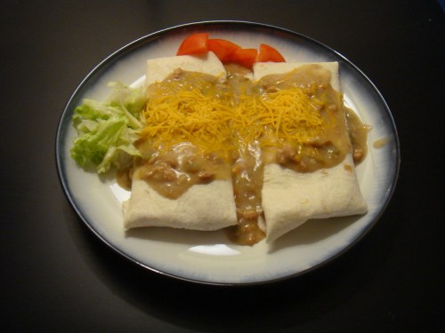 Two burritos topped with cheese and sauce, served with lettuce and tomato on a plate.
