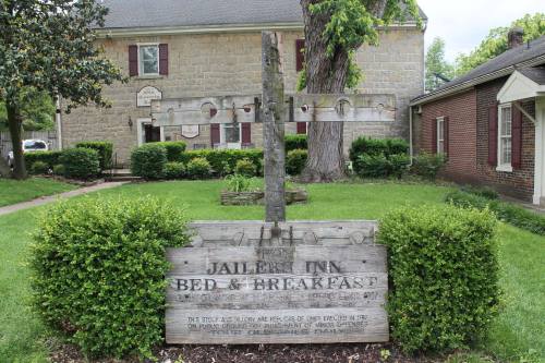 Sign for "Jailer's Inn Bed & Breakfast" in front of a stone building, surrounded by green grass and trees.