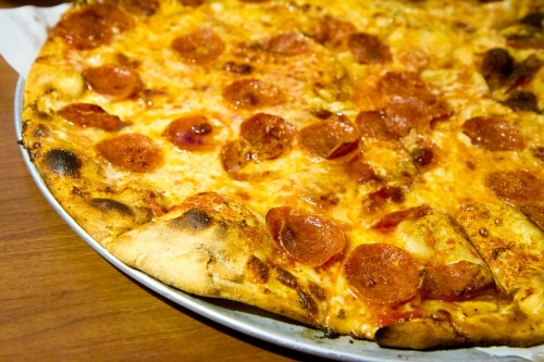 A close-up of a pepperoni pizza with a golden crust and melted cheese, served on a round metal tray.