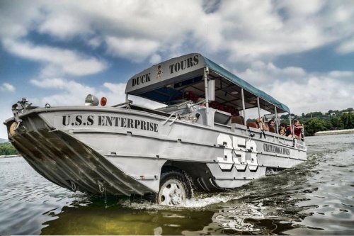 A tour boat named "U.S.S. Enterprise" on water, with passengers enjoying a scenic ride under a cloudy sky.