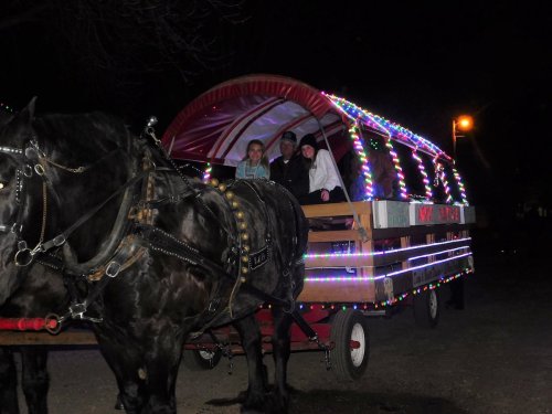 A decorated horse-drawn wagon with two children and an adult, illuminated by colorful lights at night.