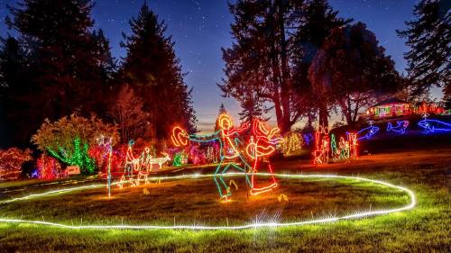 Colorful holiday lights depict dancing figures in a festive outdoor setting, surrounded by trees and a starry sky.