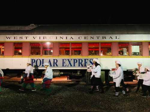 A night scene featuring the Polar Express train with chefs walking alongside it, illuminated by warm lights.