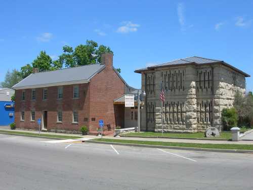 Historic buildings side by side: a brick structure and a stone building with decorative features, set against a clear blue sky.