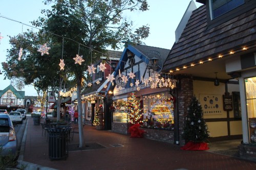 A festive street scene with shops decorated in holiday lights and snowflake ornaments, creating a cheerful atmosphere.
