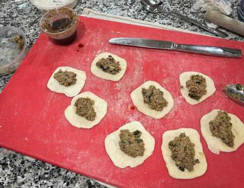 Dough circles on a red cutting board, each filled with a savory mixture, with a jar of sauce and a knife nearby.