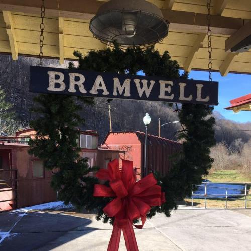 A festive wreath with a red bow hangs on a sign that reads "BRAMWELL," set against a wooded background.