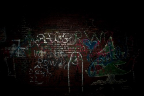 A dark brick wall covered in colorful graffiti, featuring various shapes and text.