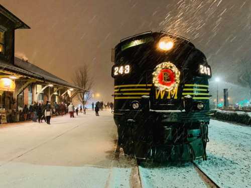 A vintage train adorned with a wreath stands on a snowy platform, with people gathered nearby in a festive atmosphere.